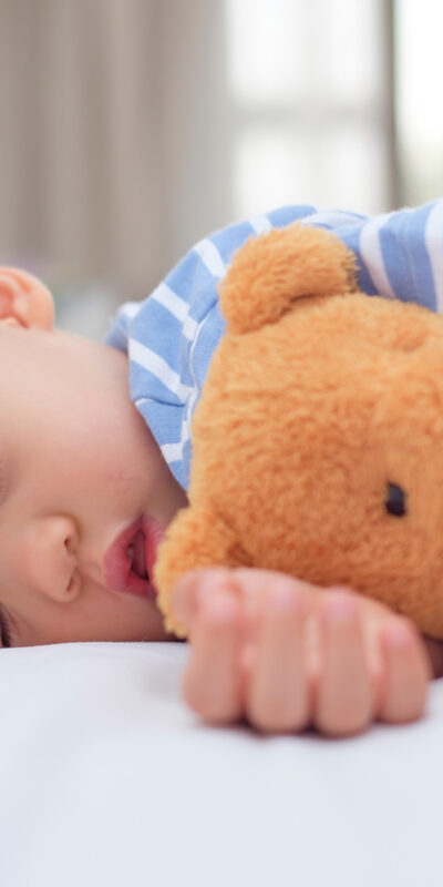 Cute healthy little Asian 18 months / 1 year old toddler baby boy child sleeping / taking a nap under blanket in bed while hugging teddy bear, Daytime sleep, kid deep sleeping, sweet dream concept
